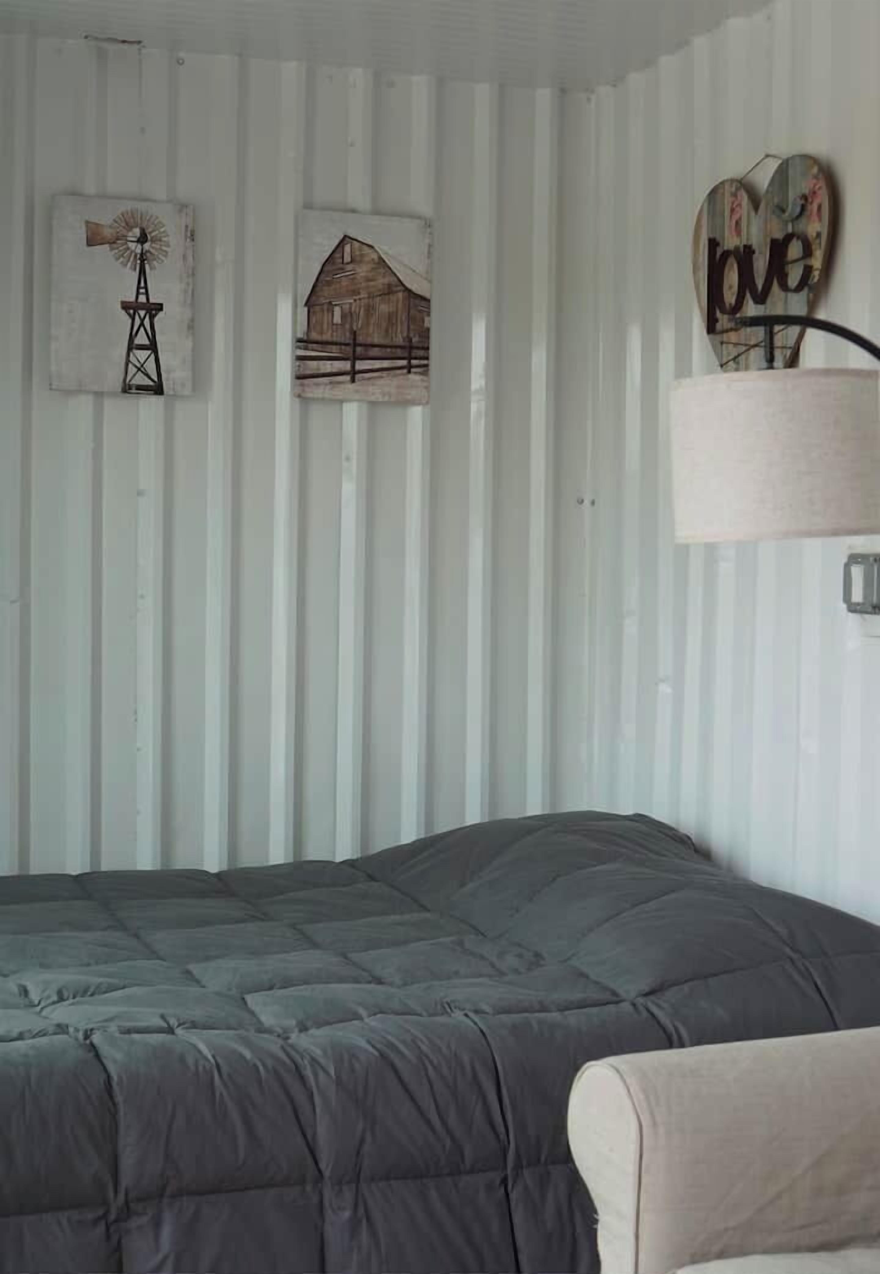 A bedroom with a bed, a lamp, and wall decorations including a windmill and a barn.