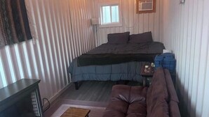A compact room with a bed, a small table, a sofa, and a window. - Gooseberry Shipping Container Room (Bandera)
