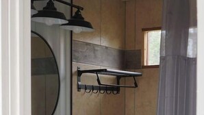 A bathroom with a white sink, a mirror, and a shower area. - Gooseberry Shipping Container Room (Bandera)