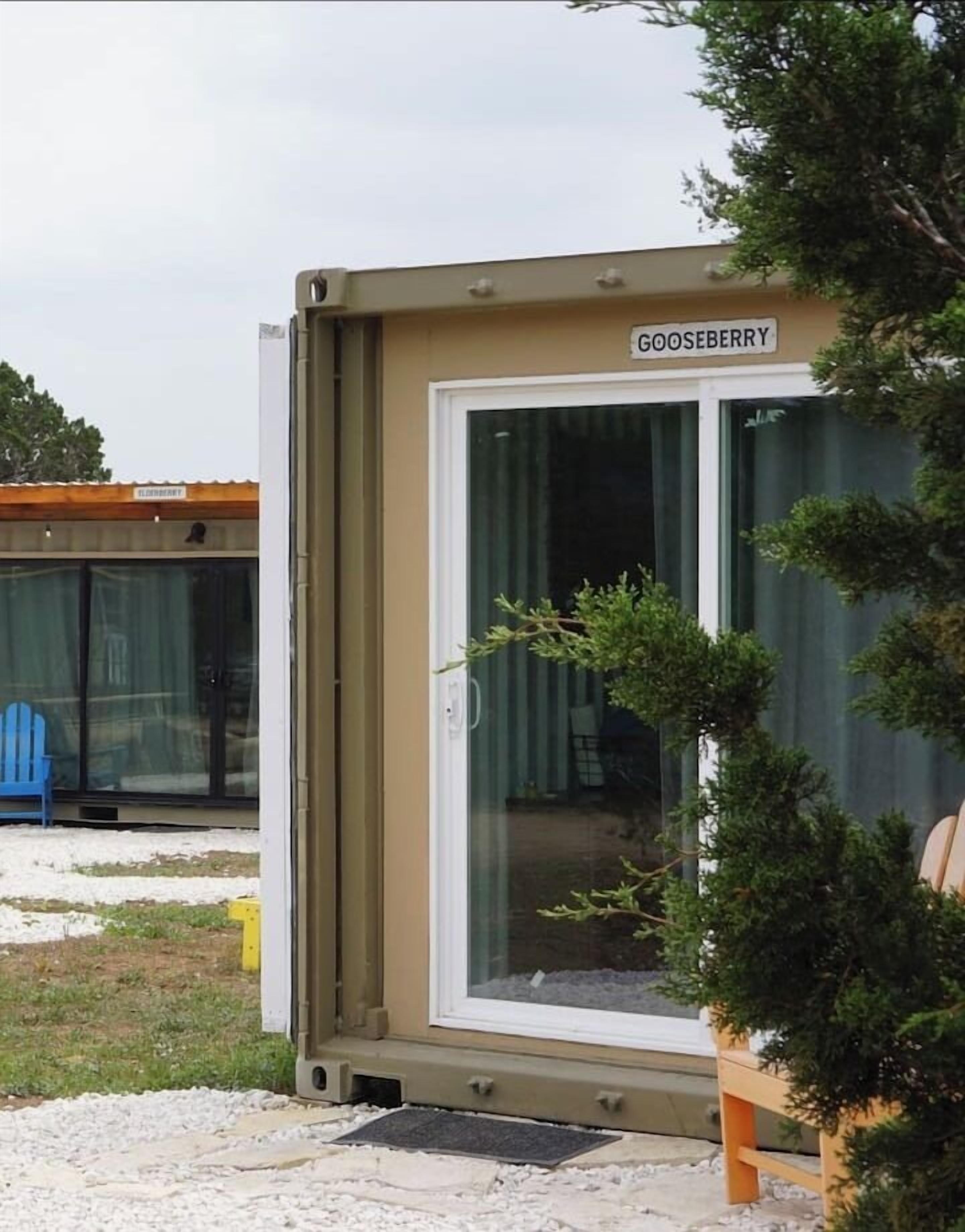 A portable container with a sliding door, labeled "GOOSEBERRY," featuring a small potted plant and a blue chair outside.