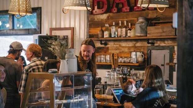 Een bar met houten planken, flessen en een kassa.