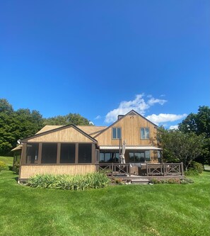 A two-story wooden house with a covered patio and a large window overlooking a well-maintained lawn. - A BEAUTIFUL 3 BEDROOM/2.5 BATH HILLTOP HOME IDEAL FOR GREAT ESCAPES,  (Chatham)