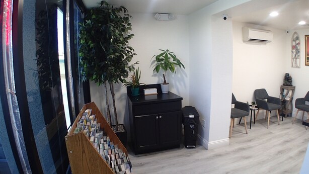 A room with a black cabinet, two potted plants, a wooden shelf with magazines, and a grey chair. - Corona Inn (Corona)