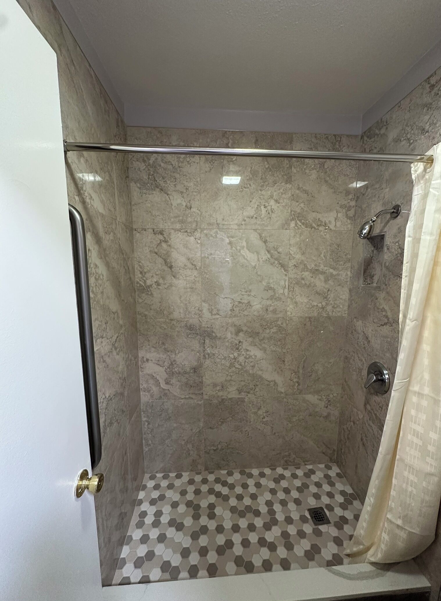 A shower with a glass door, a hexagonal tile floor, and a shower curtain.