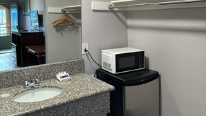 A bathroom with a granite countertop sink, a white microwave, and a mirror. - Corona Inn (Corona)