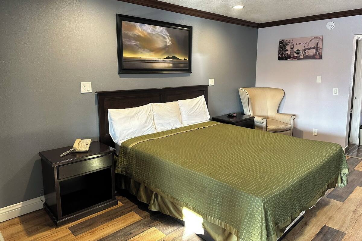 A bedroom with a bed, a chair, a nightstand, and a painting on the wall.
