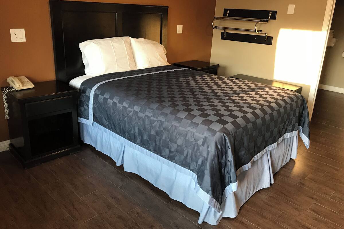A neatly made bed with a checkered bedspread and white pillows, a bedside table with a phone, and a wall-mounted shelf.