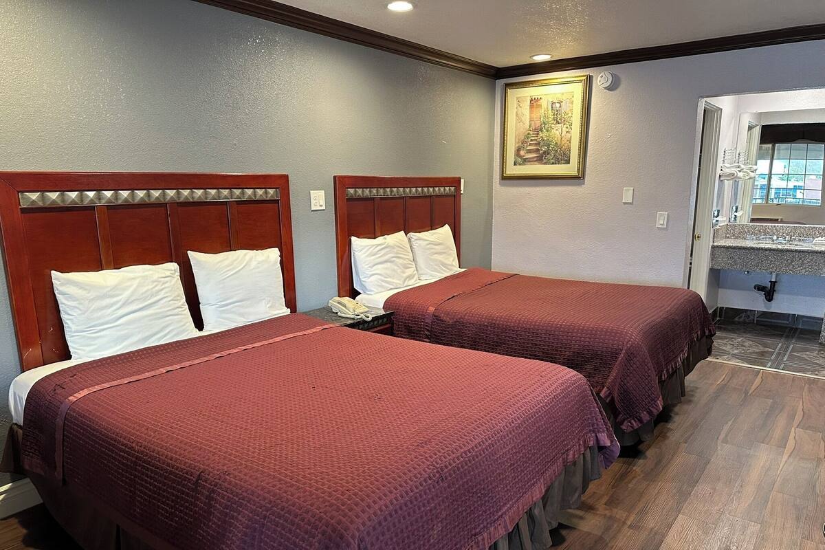A hotel room with two beds, a wooden headboard, a painting on the wall, and a view of the outside through a window.