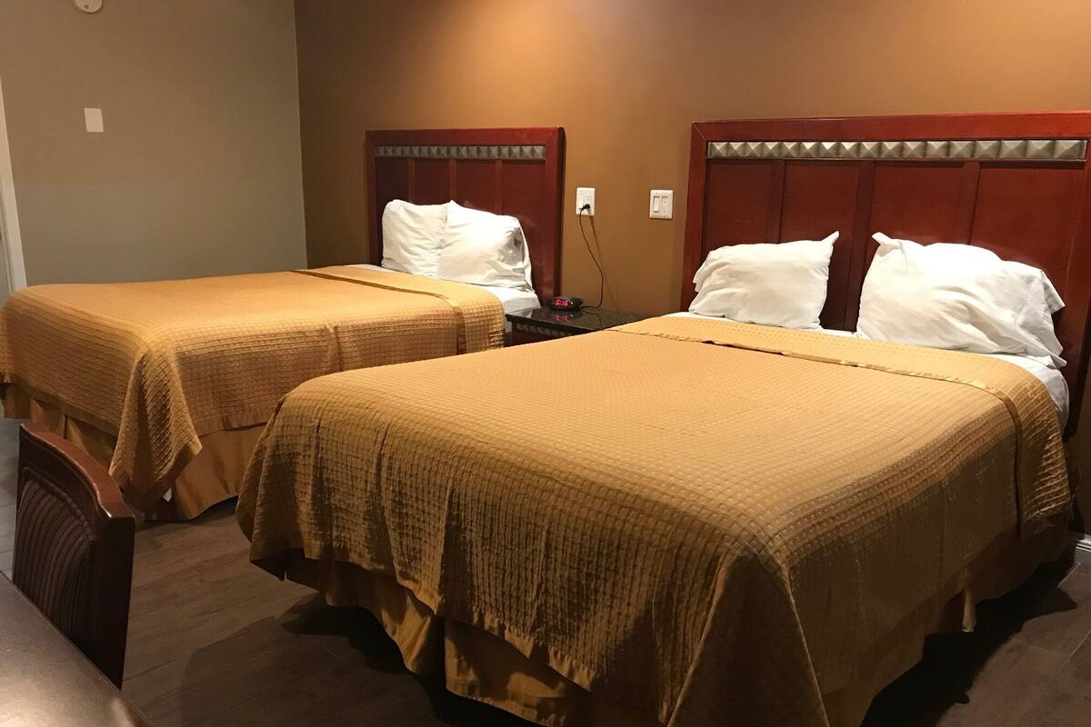 Two single beds with wooden headboards, a nightstand with a clock, and a wooden bench.