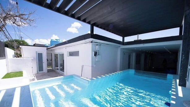 Uma piscina exterior moderna com área coberta, água azul cristalina e vista para o céu.