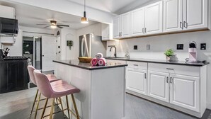 A modern kitchen with white cabinets, a stainless steel refrigerator, a black countertop, and a pink bar stool. - Spacious 5-bedroom POOL House with WiFi and AC in charming Chula Vista (Chula Vista)