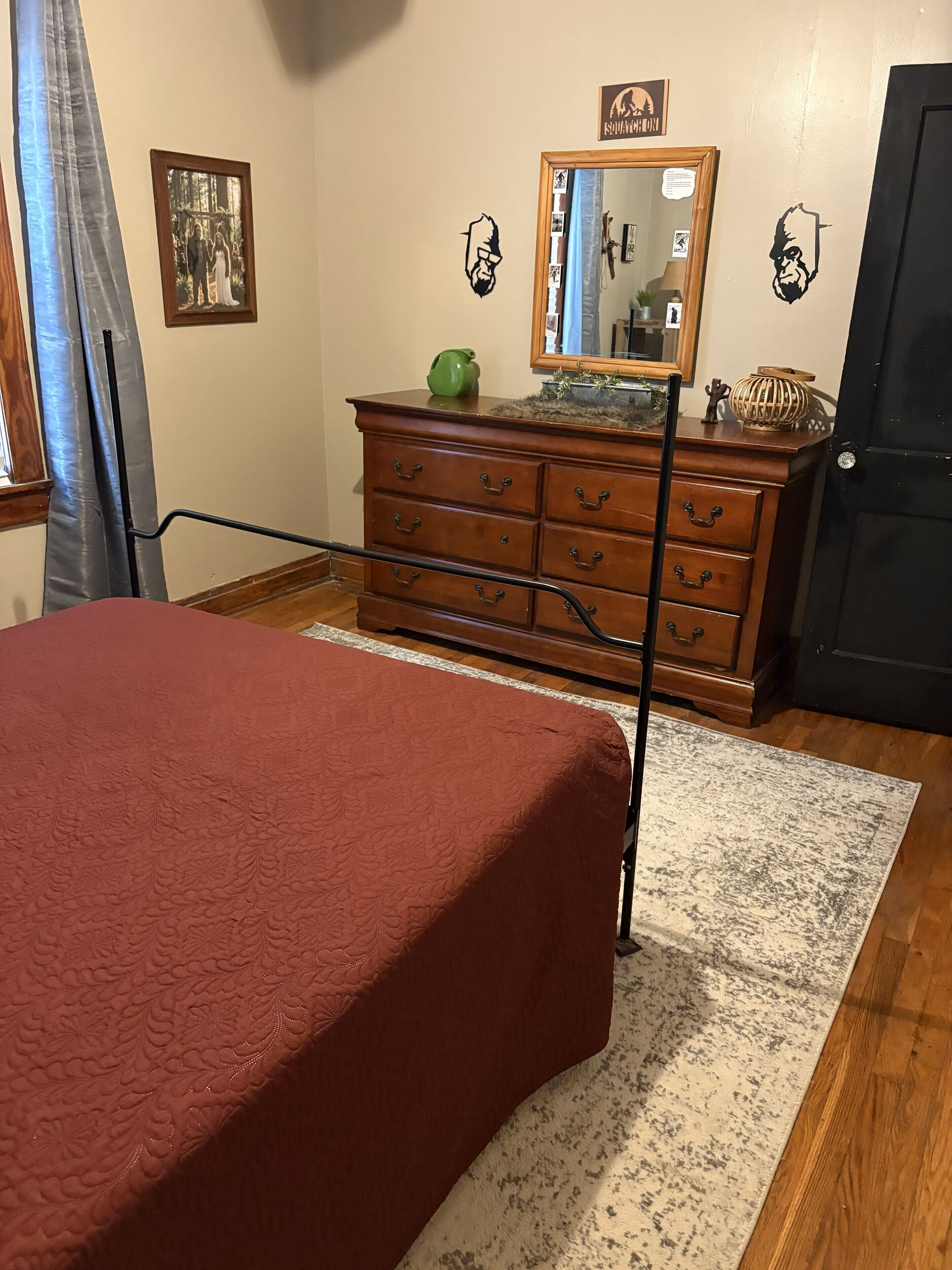 Een slaapkamer met een bed, een houten dressoir en een spiegel.