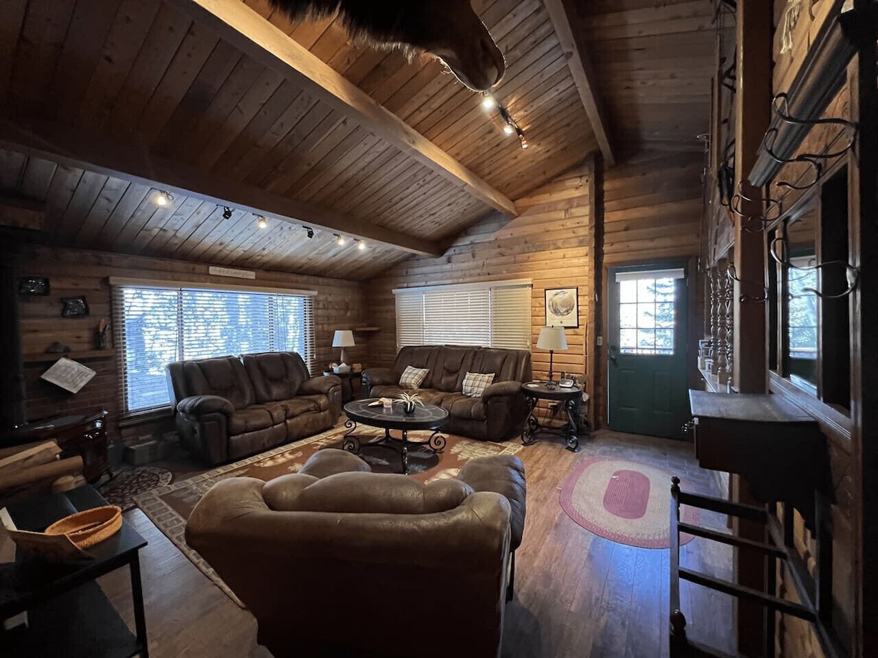 A cozy log cabin interior with a fireplace, leather sofas, and a dining area.