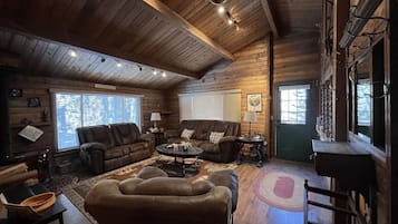 A cozy log cabin interior with a fireplace, leather sofas, and a dining area.