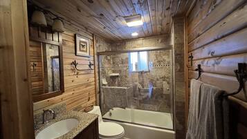 A wooden cabin bathroom with a granite sink, white toilet, and a glass-enclosed shower area.