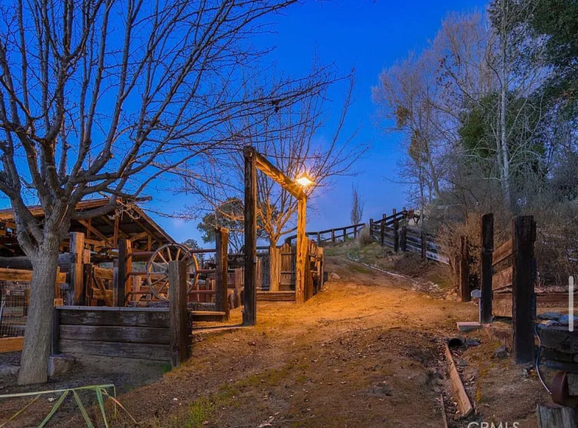 A rustic wooden structure with a wheel mechanism, surrounded by bare trees and a dirt path.