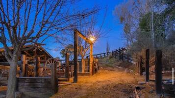 A rustic wooden structure with a wheel mechanism, surrounded by bare trees and a dirt path.