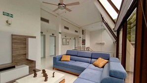 A modern living room with a blue sectional sofa, a white coffee table with decorative items, and a ceiling fan. - HOTEL KAAMU TAGANGA (Santa Marta)