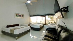 A hotel room with two beds, a sofa, a ceiling fan, a TV, and a large window. - HOTEL KAAMU TAGANGA (Santa Marta)