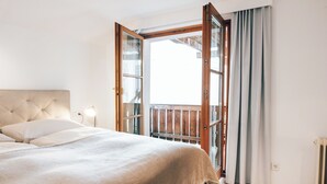 Une chambre avec un grand lit, une table de chevet, une fenêtre avec des rideaux et une vue sur un balcon.