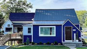 A two-story blue house with a metal roof, a front porch, and a 'Welcome' sign.