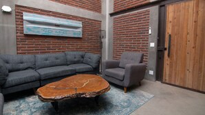 A room with a brick wall, a blue GMC logo, a gray sectional sofa, a gray armchair, and a wooden coffee table.