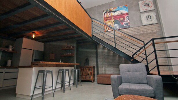 A modern kitchen with a wooden ceiling, a bar area, and a staircase leading to an upper level.