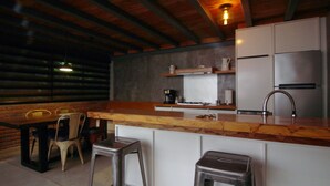 A rustic kitchen with a wooden countertop, white cabinets, and stainless steel appliances. There are two stools and a table with chairs.