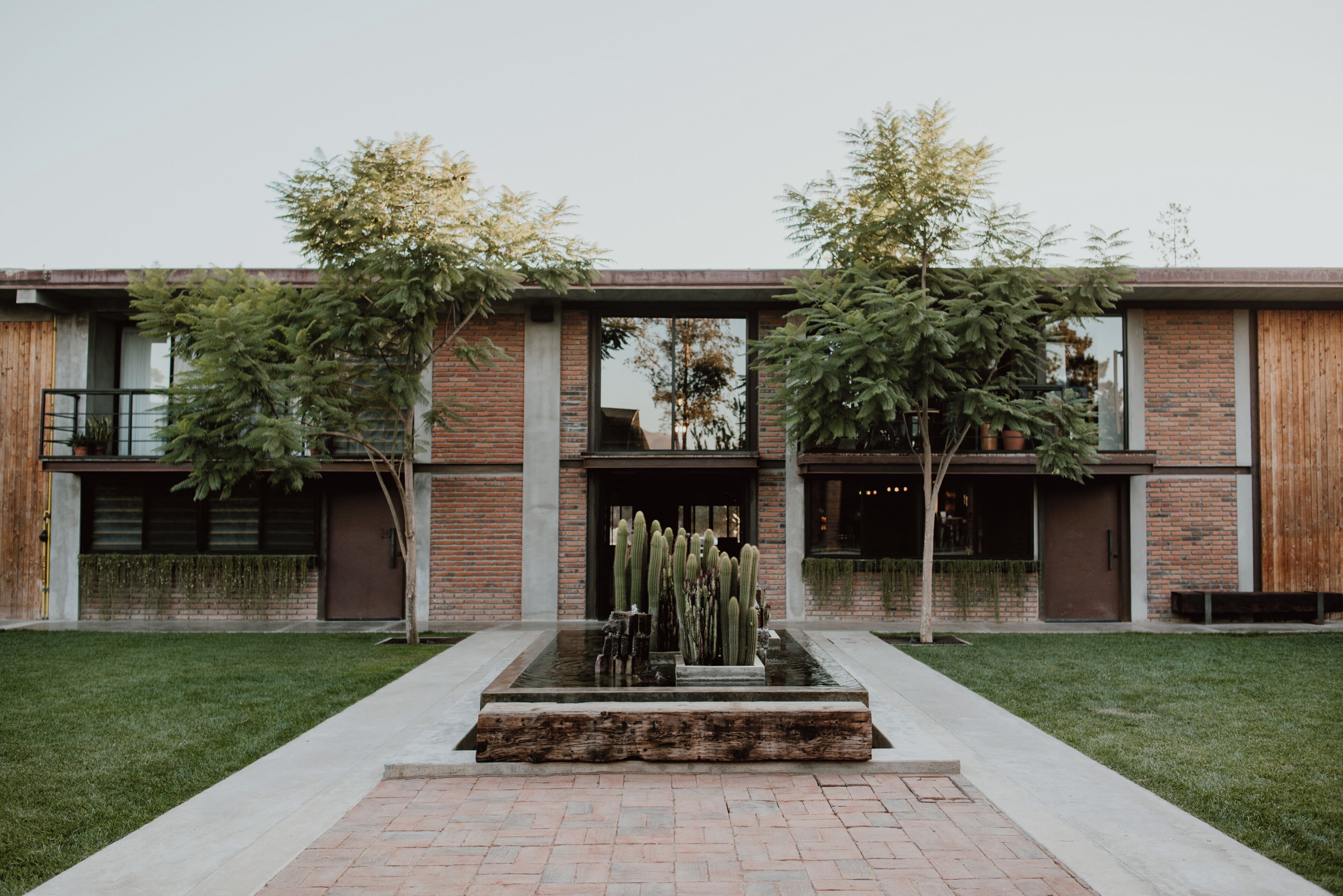 Un edificio moderno con fachada de ladrillo, un patio central con un jardín de cactus y dos árboles.