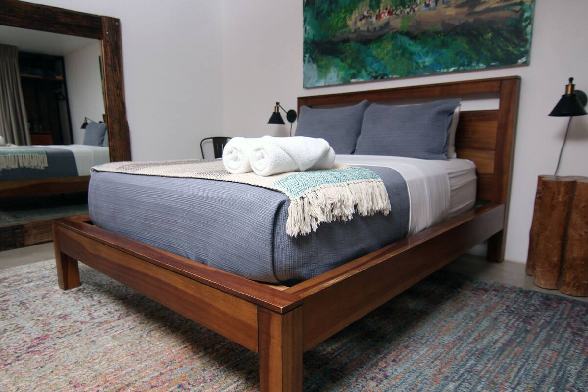 Un lit bien fait, recouvert d’une couvre-lit bleue et blanche, avec une tête de lit en bois et un tableau accroché au-dessus.