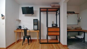 A compact room with a wooden desk, a black chair, a TV mounted on the wall, and a bunk bed with a mattress on top.