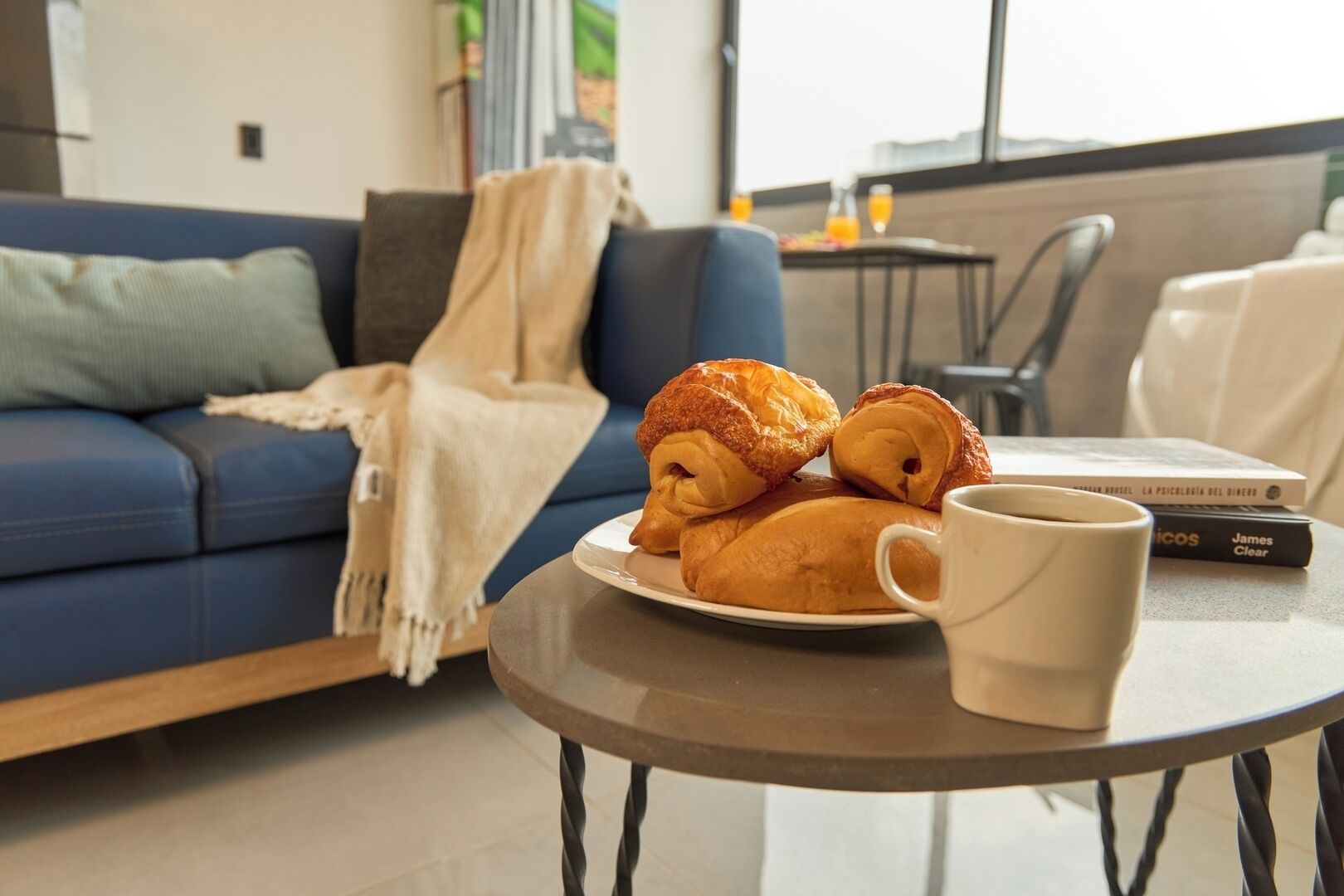 A cozy living room with a blue sofa, a white blanket, and a plate of croissants on a small table.