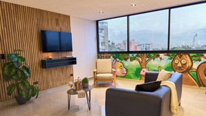 A modern living room with a large window, a flat-screen TV, a sofa, a chair, and a small table with a plant and a bottle. - Cozy Getaway Rosa Negra Stadio Suite (Medellín)