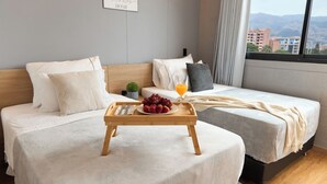 A hotel room with two beds, a tray with fruit and juice, and a city view through the window. - Cozy Getaway Rosa Negra Stadio Suite (Medellín)