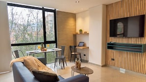 A modern living room with a sofa, a dining table, and a TV mounted on a wooden wall. - Rosa Negra Comfort Suite Stadio Aparta (Medellín)