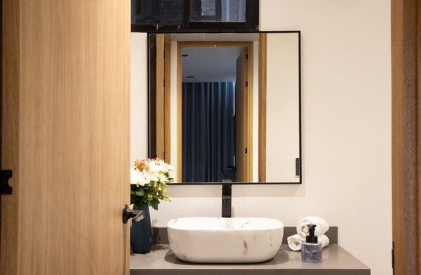 Une salle de bain avec un lavabo en marbre blanc, un miroir et un vase de fleurs.