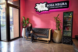 A woman sitting on a black leather sofa in front of a pink wall with a neon sign reading "ROSA NEGRA APARTMENTS". - Luxurious Jacuzzi Aparta-suite Stadio Rosa Negra (Medellín)