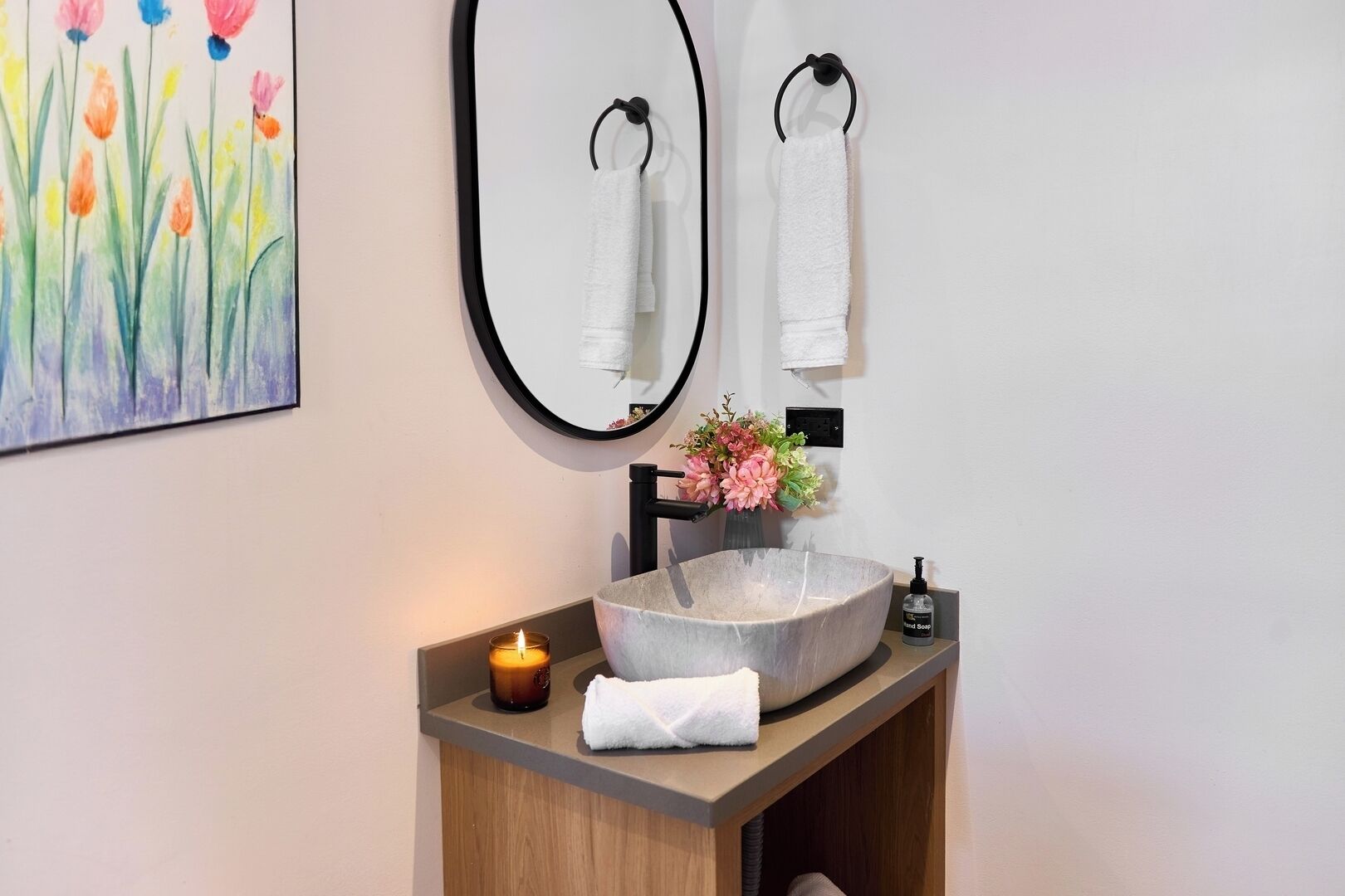 Un bagno con un lavandino di pietra rotondo, uno specchio, due asciugamani, una candela e un vaso di fiori.