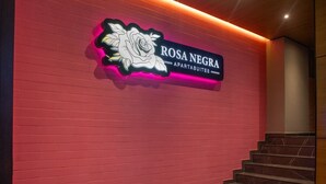 A sign for 'ROSA NEGRA APARTS SUITES' with a neon rose design, a staircase, and a red brick wall. - Comfy Aparta-suite Stadio Rosa Negra (Medellín)