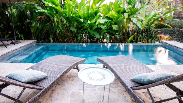 A swimming pool with two wicker lounge chairs and a small table, surrounded by lush greenery. - Mountain View, Saltwater Pool, Kitchen, A/C, King Bed, Fast WiFi - “Montaña” (San Francisco)