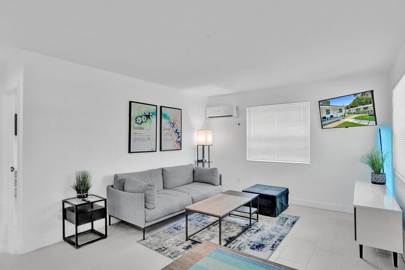 A modern living room with a grey sofa, a coffee table, a side table with a plant, and a TV on the wall.