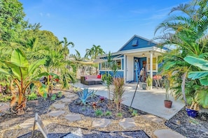 A house with a blue roof, a porch, and a garden with various plants and a seating area. - Zen 2br, 7 Min From Beach & Airport, Save Now! (Dania Beach)