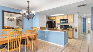 A modern kitchen with a central island, a dining area with wooden chairs, and a chandelier. - 3-br Condo Near Disney Family-friendly Retreat (Kissimmee)