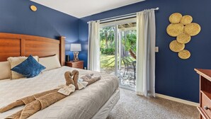 A bedroom with a large bed, a wooden headboard, a nightstand with a lamp, and a view of the outdoors through a glass door. - 3-br Condo Near Disney Family-friendly Retreat (Kissimmee)