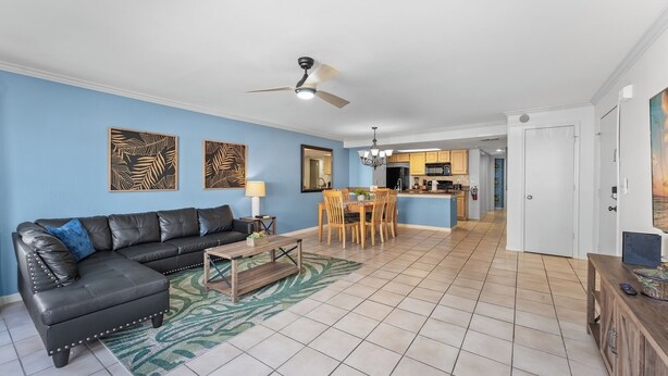 A living room with a black leather sofa, a wooden coffee table, and a dining area with wooden chairs and a table. There is a kitchen in the background with a microwave and stove. - 3-br Condo Near Disney Family-friendly Retreat (Kissimmee)