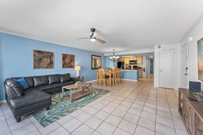A living room with a black leather sofa, a wooden coffee table, and a dining area with wooden chairs and a table. There is a kitchen in the background with a microwave and stove. - 3-br Condo Near Disney Family-friendly Retreat (Kissimmee)