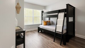 A bunk bed room with a desk, a hanging light fixture, and a window with blinds.