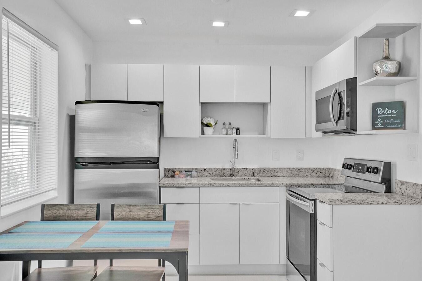 Una cocina moderna con armarios blancos, un refrigerador de acero inoxidable, un microondas y un horno empotrado.