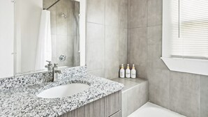 A modern bathroom with a granite countertop sink, a shower, and a window with blinds. - Spacious 4BR Getaway: Perfect for Family & Friends (Detroit)