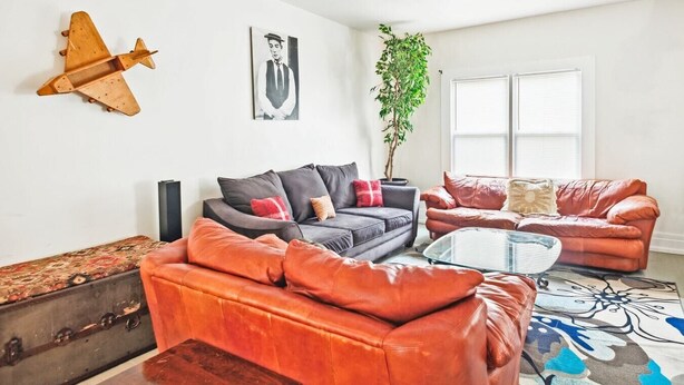 A modern living room with a grey sofa, a red sofa, a glass coffee table, and a large plant. - Spacious 4BR Getaway: Perfect for Family & Friends (Detroit)